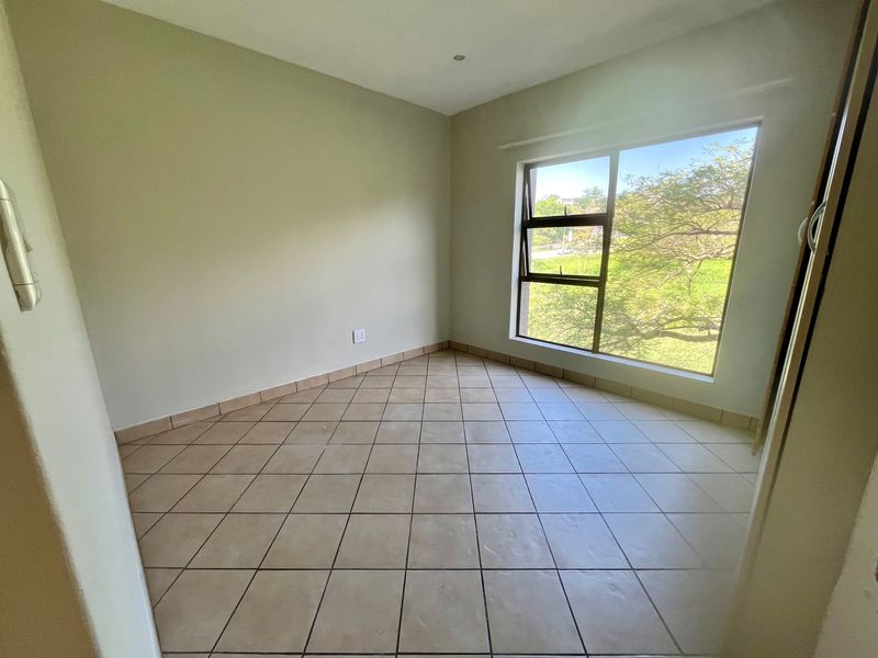 An empty bedroom featuring neutral wall paint, tiled flooring, and a large window providing natural light and garden views.