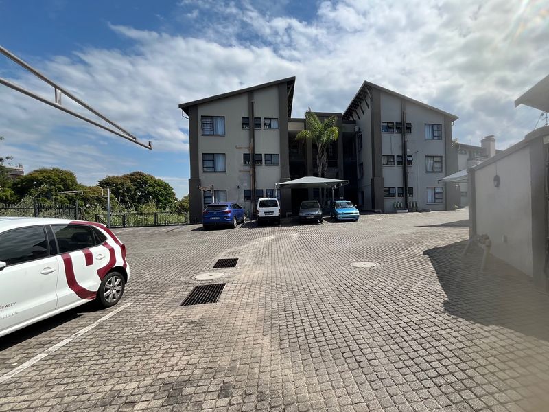 Exterior view of an apartment complex featuring a paved parking area, covered carport, and multi-story building facade.