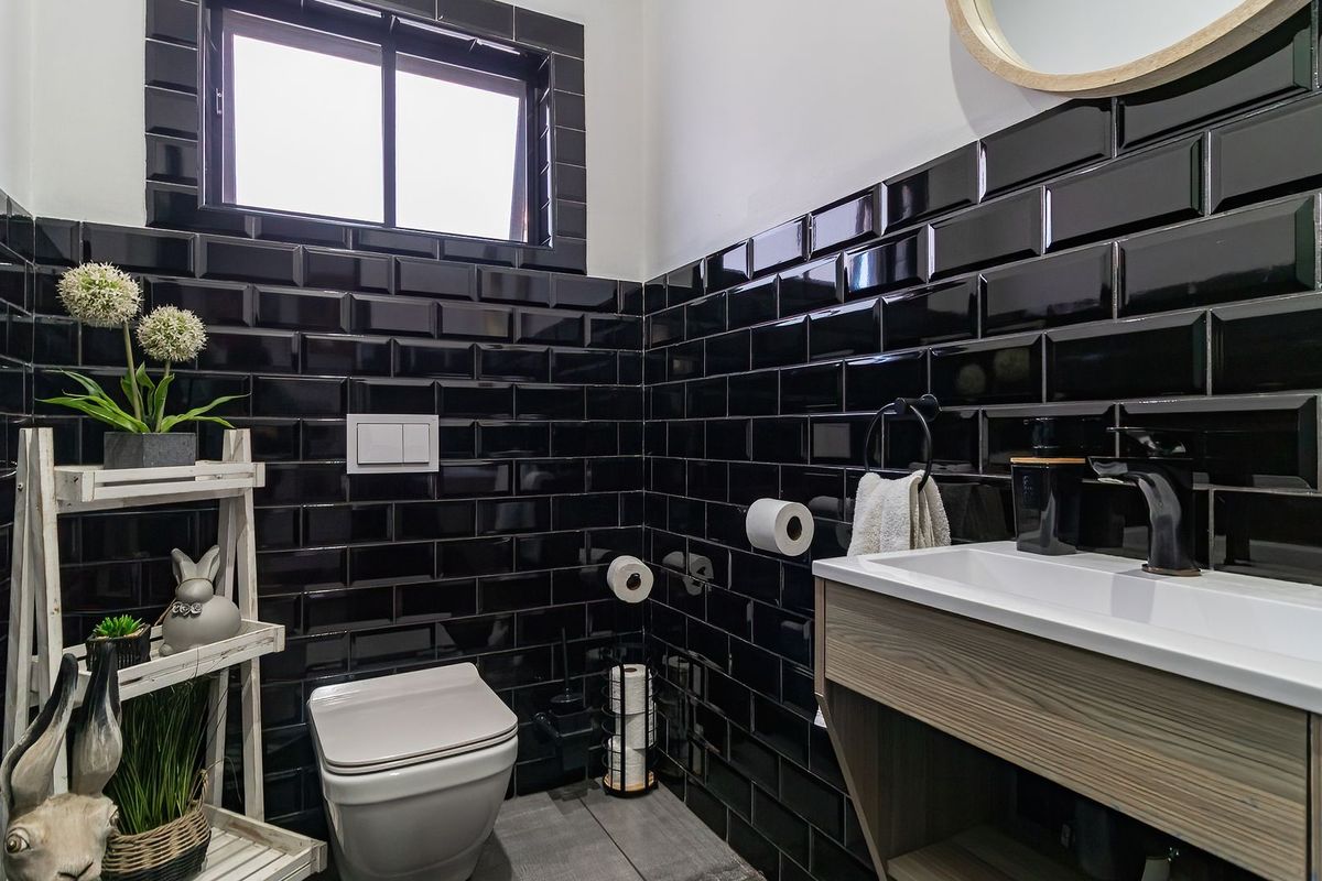 Modern bathroom featuring striking black subway wall tiles, a wall-mounted toilet with a flush plate, and a contemporary vanity unit with black tapware.