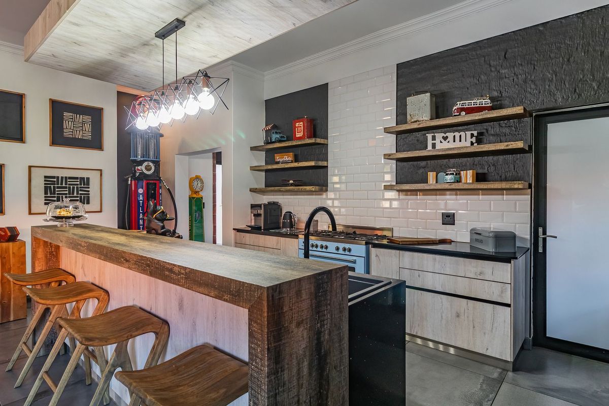 Modern kitchen featuring a breakfast bar, subway tile backsplash, floating timber shelving, and high-quality built-in cabinetry with integrated gas cooking appliances.