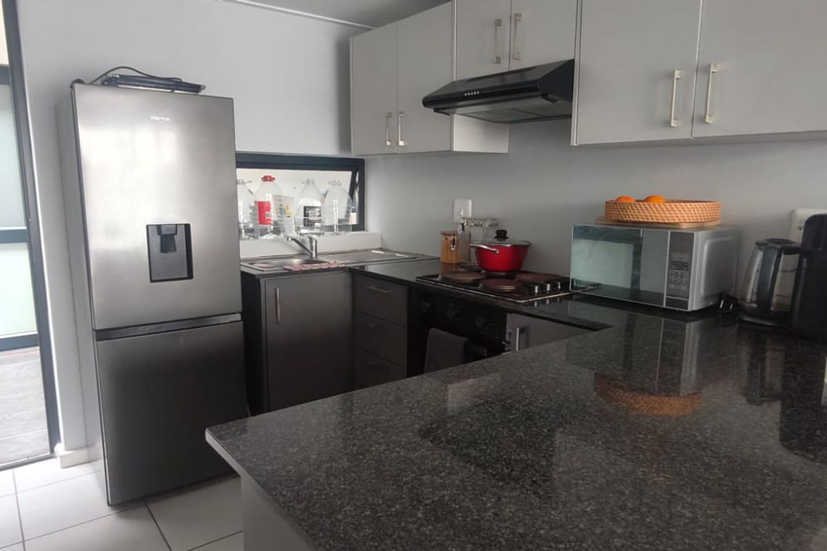 A functional kitchen featuring granite countertops, built-in cabinetry, and integrated appliances, with direct access to an outdoor patio area.
