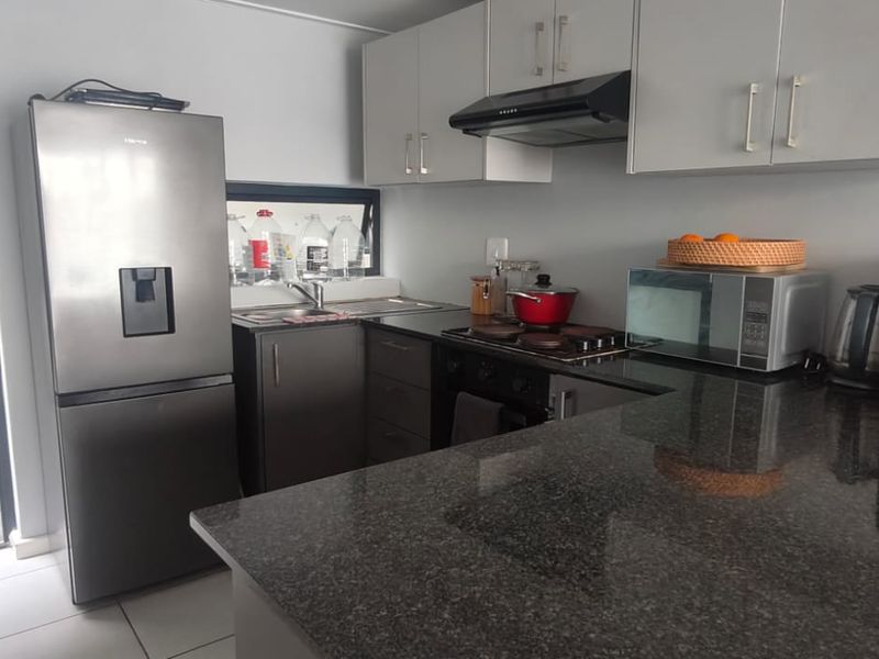 A functional kitchen featuring granite countertops, built-in cabinetry, and integrated appliances, with direct access to an outdoor patio area.