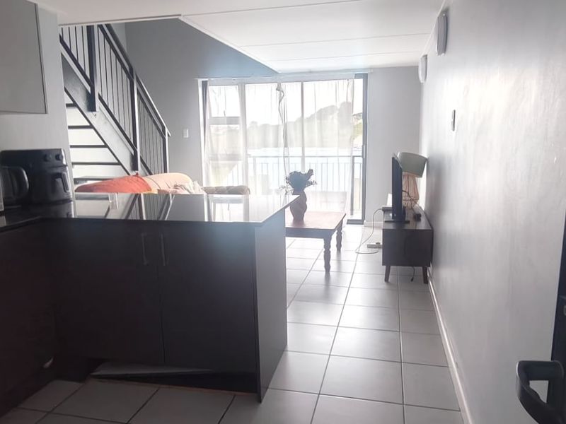 Open-plan living area featuring a kitchen with granite countertops, tiled flooring, and a staircase leading to the upper level with access to a balcony.