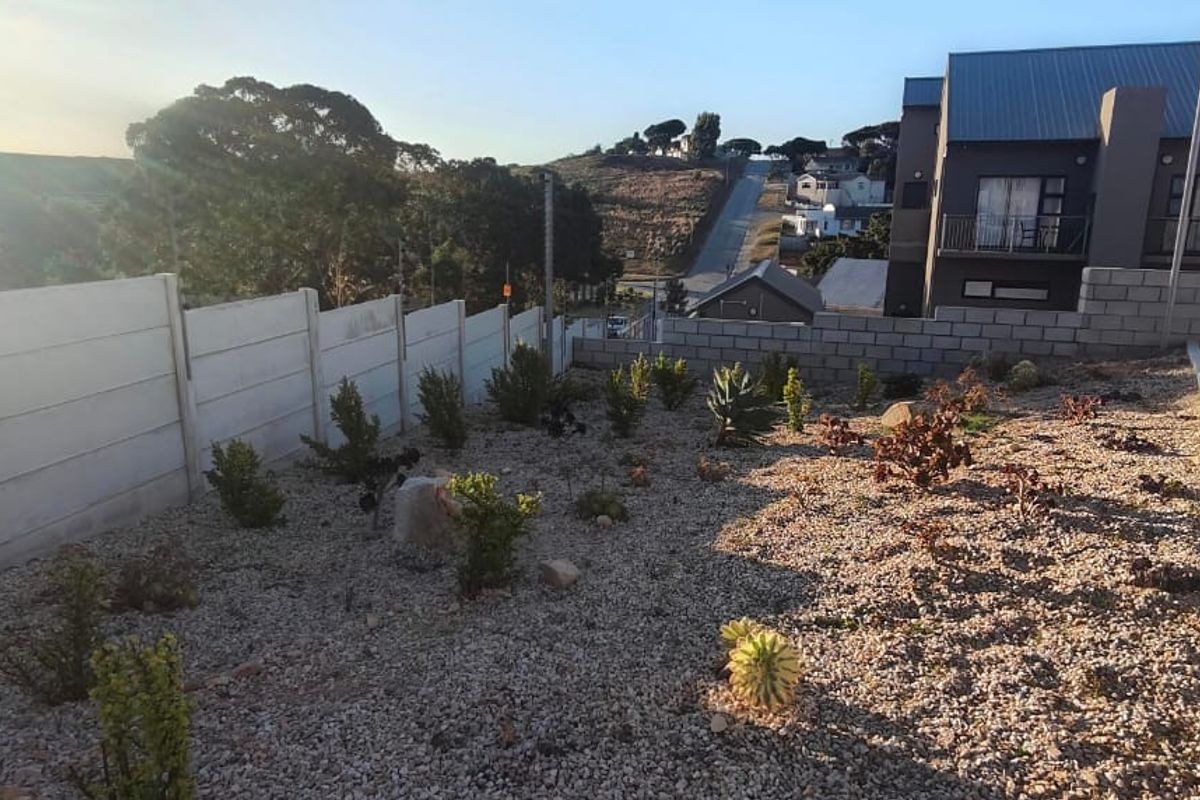 A rear exterior view showing a gravel landscaped garden area, precast concrete boundary wall, and adjacent paved driveway.