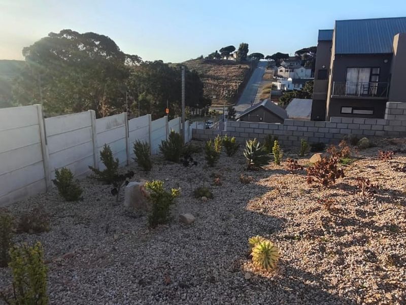 A rear exterior view showing a gravel landscaped garden area, precast concrete boundary wall, and adjacent paved driveway.