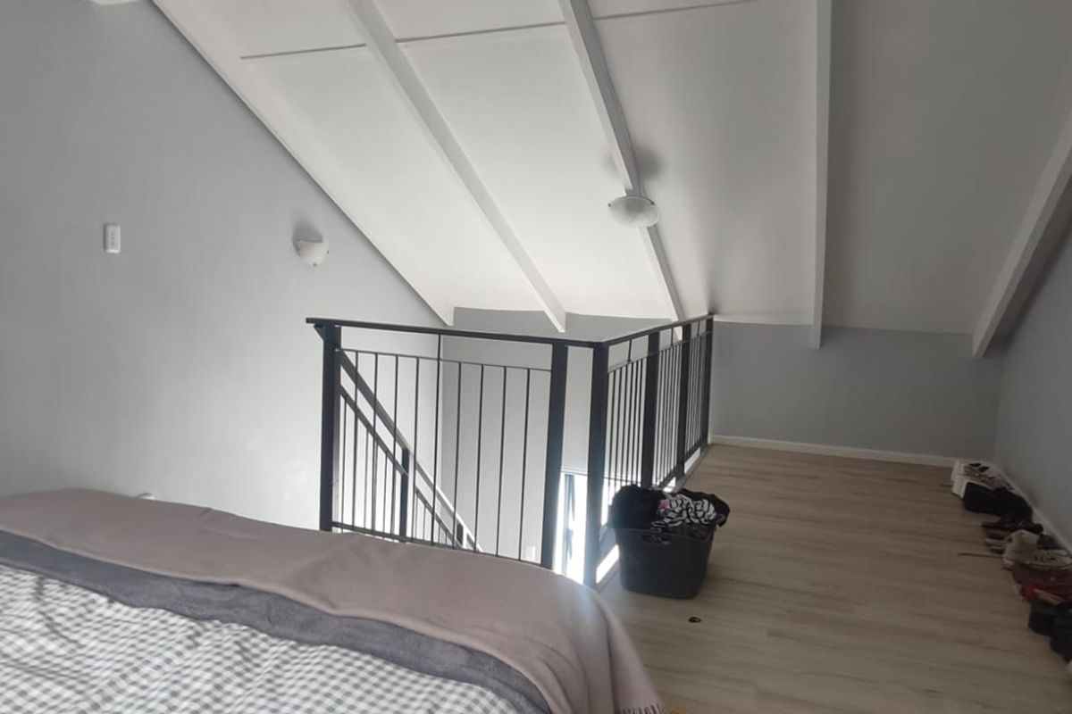 A loft-style bedroom featuring vaulted ceilings with exposed rafters, laminate flooring, and a metal balustrade overlooking the lower level.