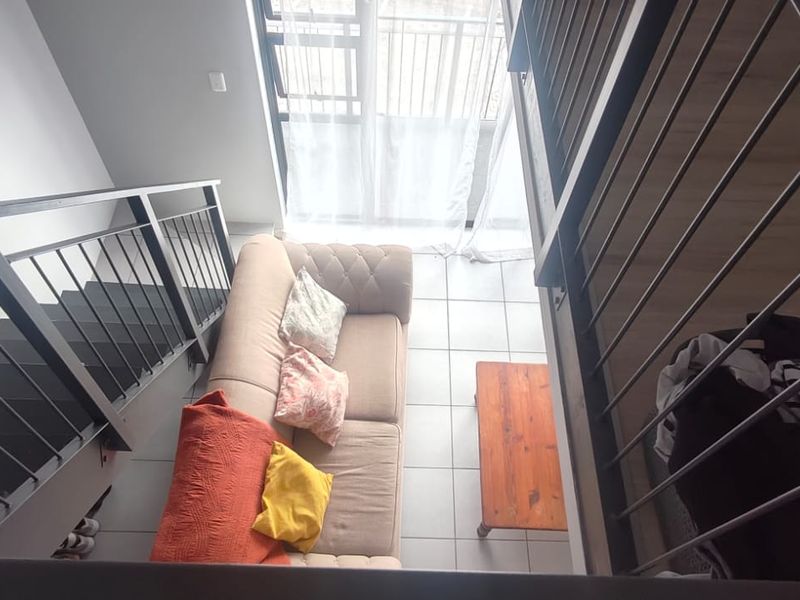 An elevated view of a living area featuring a metal staircase, tiled flooring, and access to a balcony through a sliding glass door.