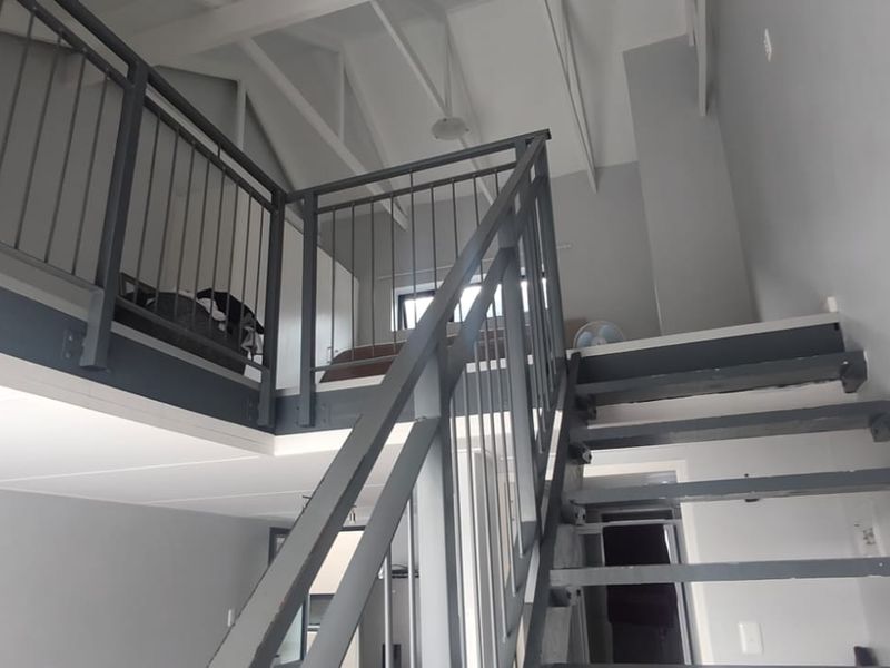A bright living area featuring a mezzanine level, vaulted ceilings with exposed rafters, and a modern metal staircase with a matching balustrade.