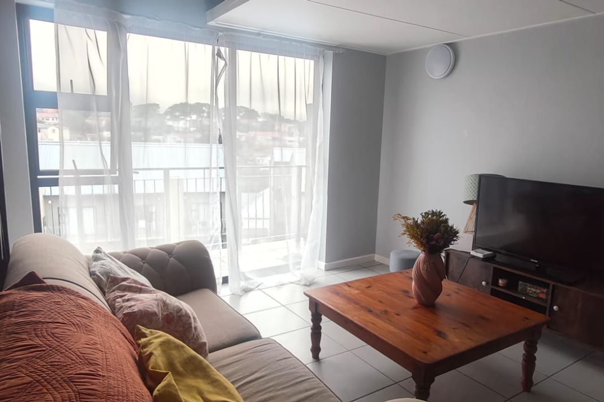 A bright living room featuring tiled flooring, a staircase, and large sliding glass doors providing access to a balcony.