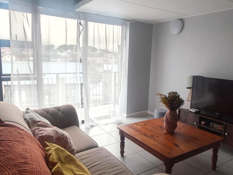 A bright living room featuring tiled flooring, a staircase, and large sliding glass doors providing access to a balcony.