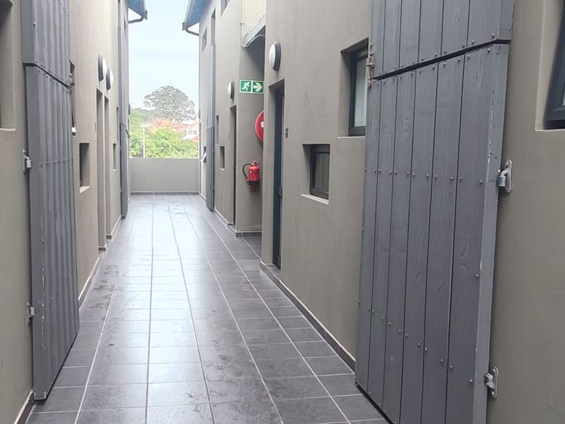 A clean, tiled outdoor apartment hallway featuring grey wall finishes, secure door access, and essential fire safety equipment.