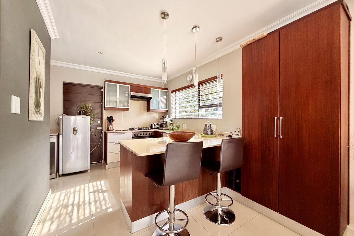 A well-maintained kitchen featuring warm wood cabinetry, stone countertops, a breakfast bar, and integrated gas hob with extractor fan.