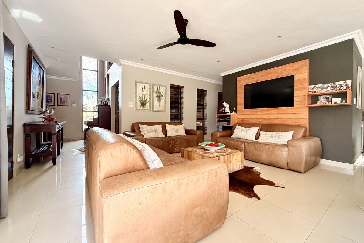 Spacious living room featuring tiled flooring, a timber feature wall, ceiling fan, and large double-height windows providing ample natural light.