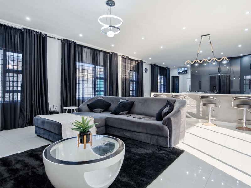 A modern open-plan living and kitchen area featuring sleek cabinetry, a central island, tiled floors, and contemporary lighting fixtures.