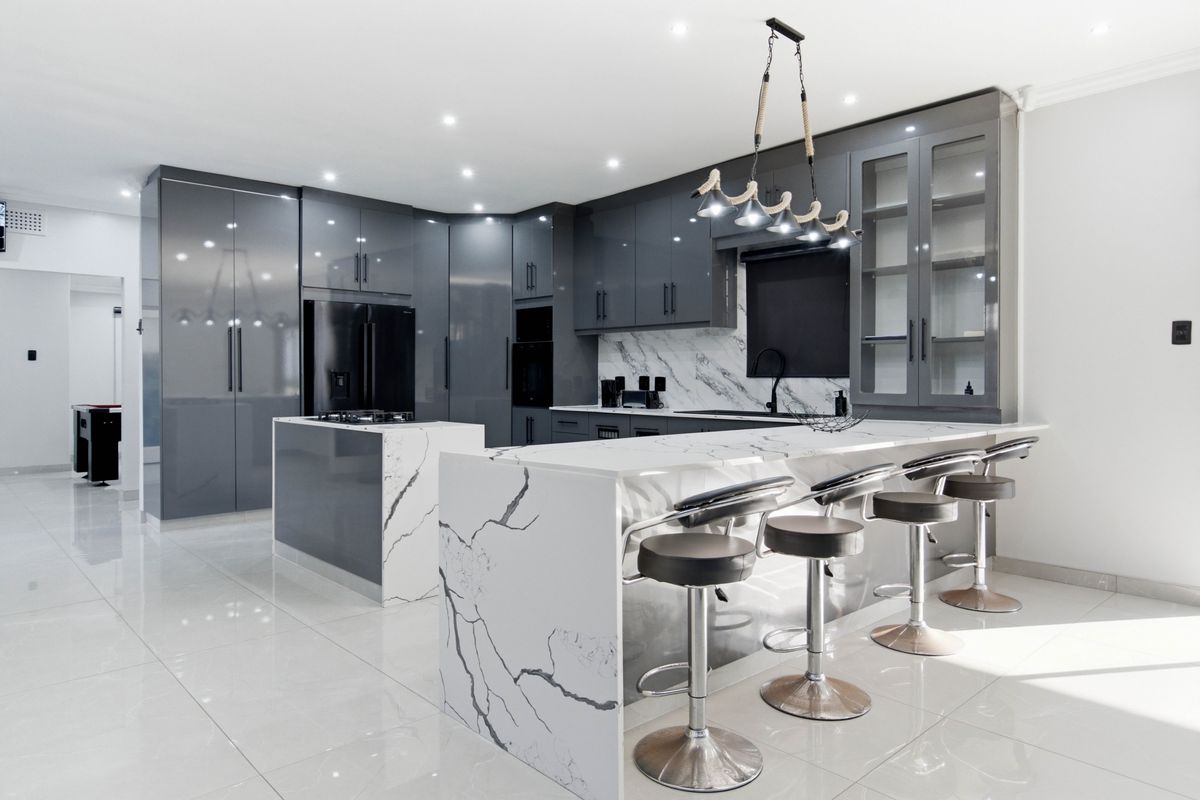 Modern kitchen featuring high-gloss grey cabinetry, marble-look quartz countertops, a central island, and premium built-in appliances with sleek, contemporary finishes.
