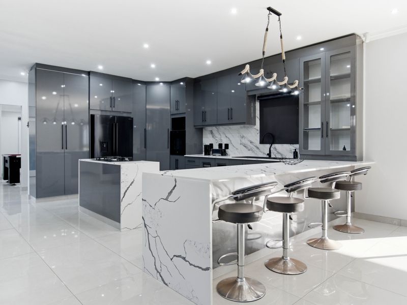 Modern kitchen featuring high-gloss grey cabinetry, marble-look quartz countertops, a central island, and premium built-in appliances with sleek, contemporary finishes.