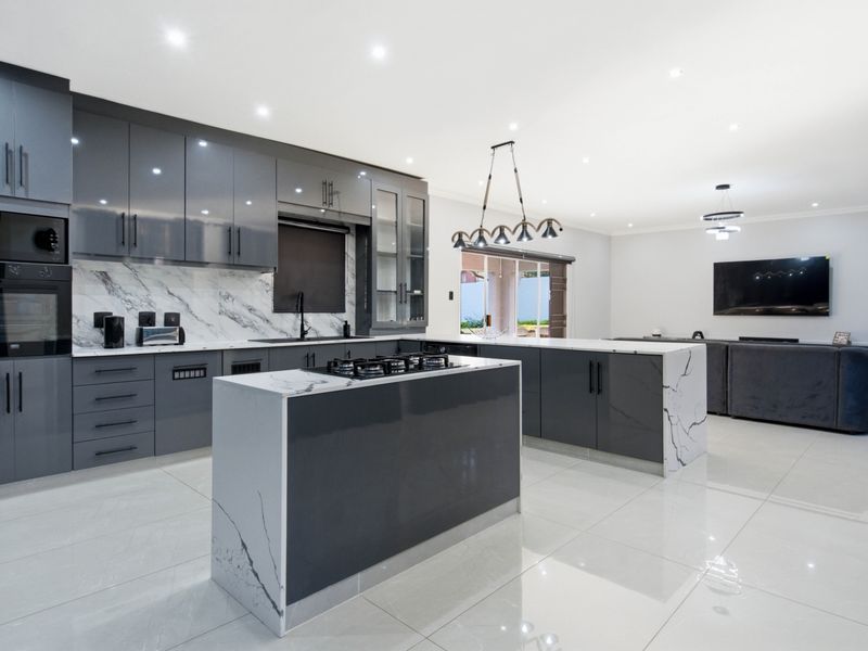 Modern open-plan kitchen and living area featuring high-gloss cabinetry, marble-look stone countertops, integrated appliances, and sleek porcelain floor tiles.