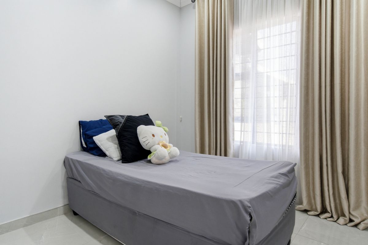 A clean and well-maintained bedroom featuring neutral wall tones, tiled flooring, and a window fitted with security bars and full-length curtains.