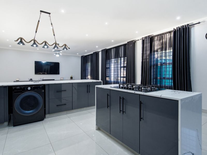 Modern kitchen featuring a central island with a gas hob, sleek dark cabinetry, marble-look countertops, and polished porcelain floor tiles.