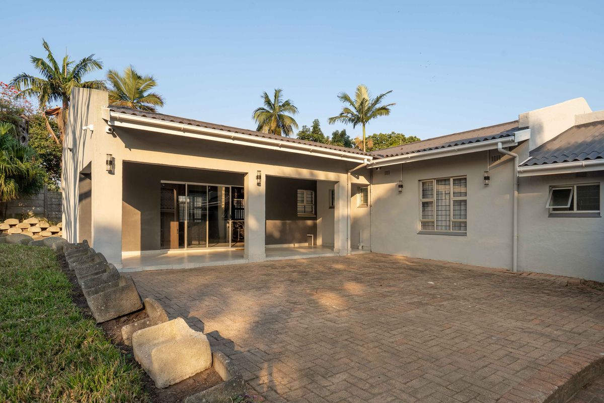 A well-maintained rear exterior featuring a spacious covered patio, paved courtyard area, and secure window fixtures under a tiled roof.
