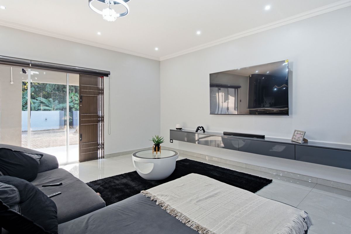 Modern living room featuring tiled floors, recessed lighting, a sleek floating media console, and a sliding glass door providing access to the outdoor area.