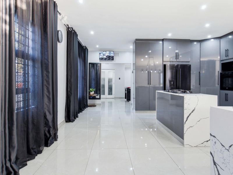 Modern kitchen featuring high-gloss grey cabinetry, a striking marble-look island with integrated cooktop, and polished porcelain floor tiles throughout.
