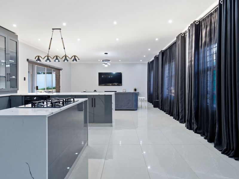 Modern open-plan kitchen and living area featuring a large island with gas hob, sleek cabinetry, quartz countertops, and polished porcelain flooring.