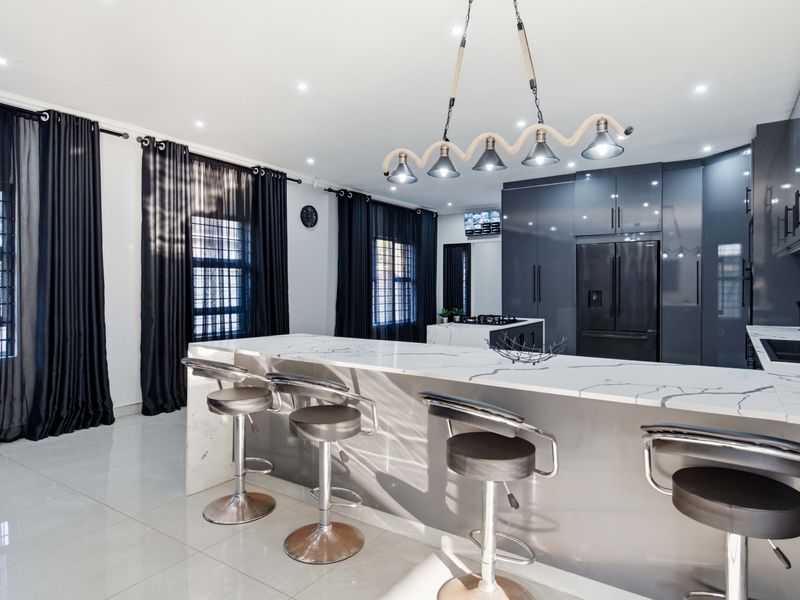 Modern open-plan kitchen featuring a marble-look waterfall island bench, sleek glossy grey cabinetry, and recessed downlighting in a contemporary living space.