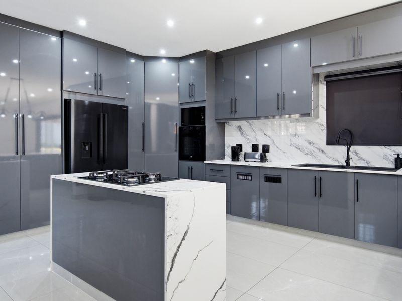 Modern kitchen featuring high-gloss grey cabinetry, marble-look stone island with integrated gas cooktop, built-in appliances, and sleek black fixtures.