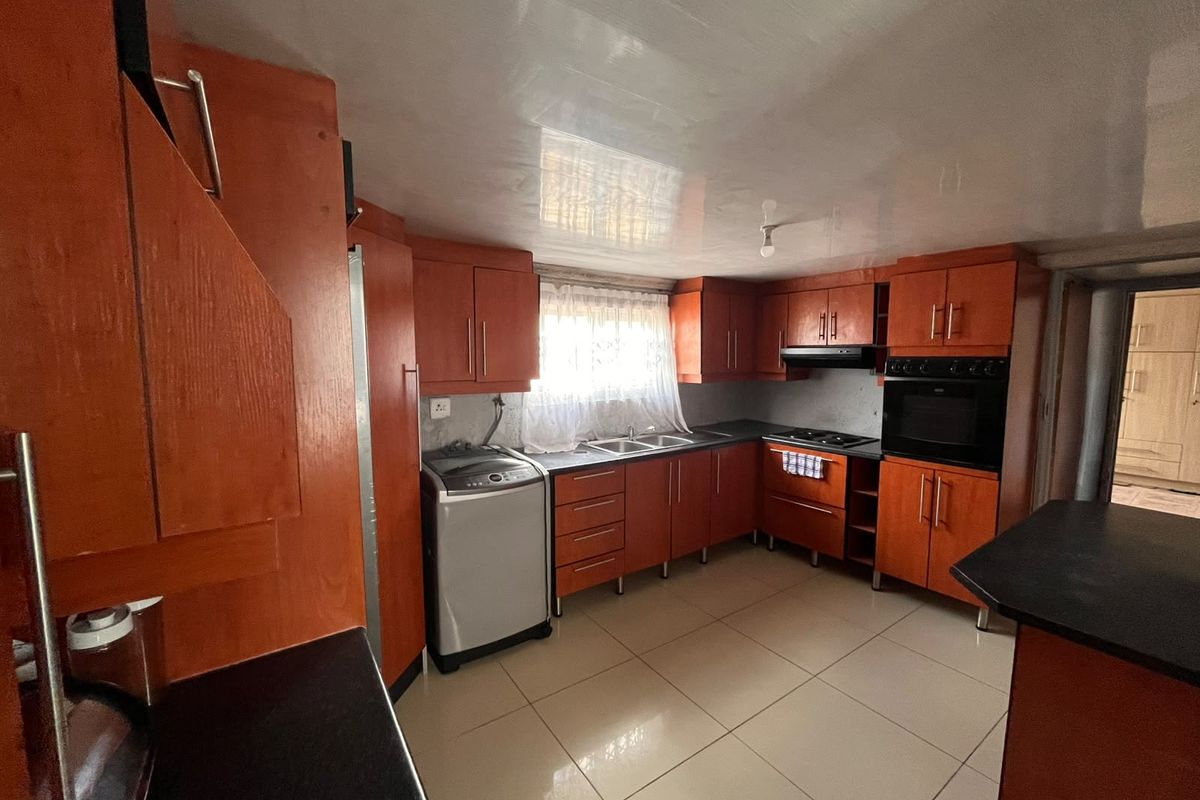 A functional kitchen featuring built-in wooden cabinetry, integrated oven and hob, double sink, and tiled flooring, offering a practical layout for daily use.