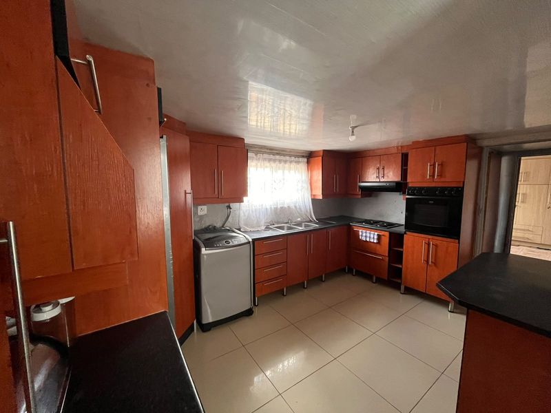 A functional kitchen featuring built-in wooden cabinetry, integrated oven and hob, double sink, and tiled flooring, offering a practical layout for daily use.