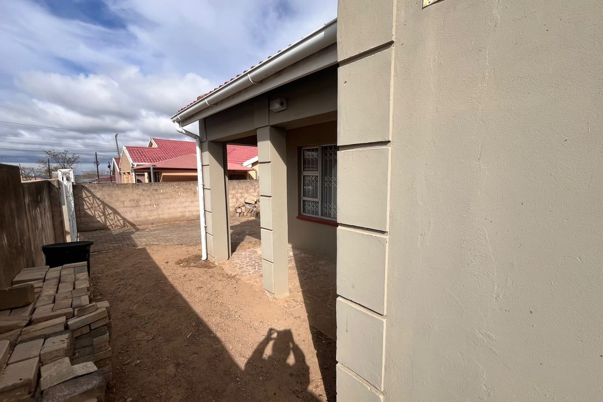 A view of the rear exterior of the house featuring a covered patio area, security bars on windows, and a paved side yard.