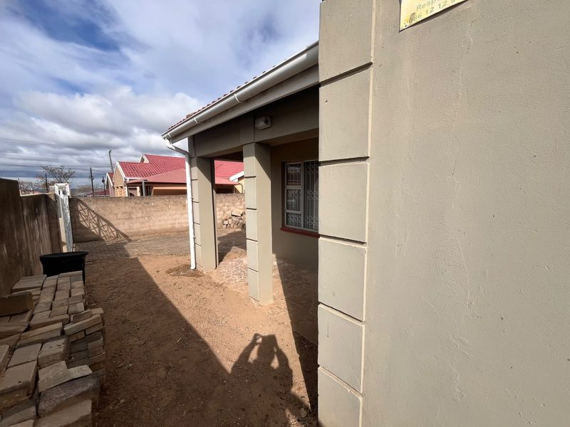 A view of the rear exterior of the house featuring a covered patio area, security bars on windows, and a paved side yard.