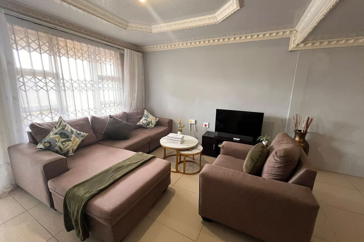 A living room featuring tiled flooring, decorative ceiling cornicing, and a large window fitted with a security gate.