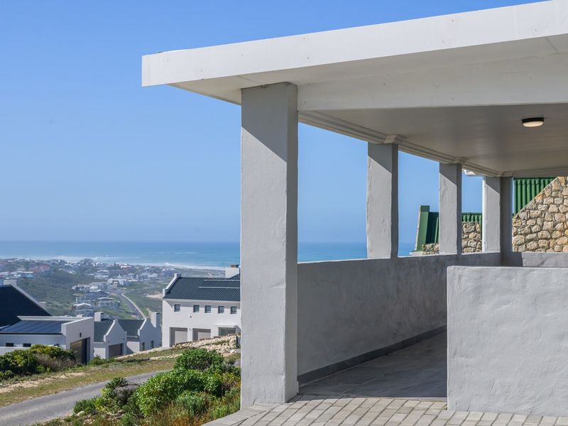 A spacious covered patio featuring paved flooring and stone masonry accents, offering expansive coastal and neighborhood views.