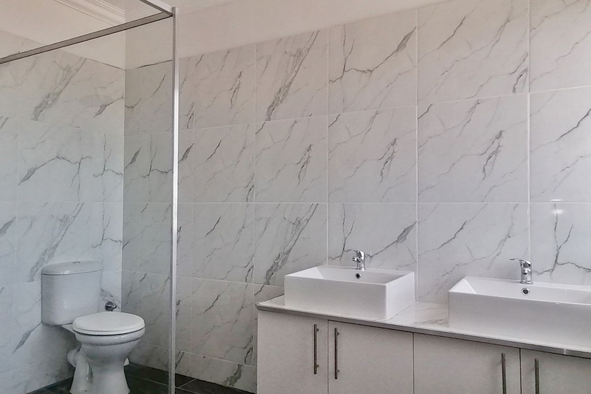 Modern bathroom featuring a double vanity with under-counter storage, a glass-enclosed shower, and elegant marble-look wall tiling.