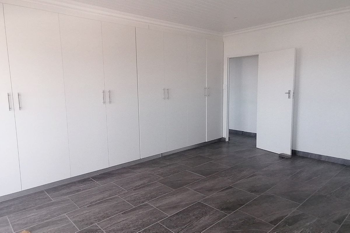 A clean, empty bedroom featuring modern dark grey floor tiles and extensive white built-in cupboards with a neutral finish.