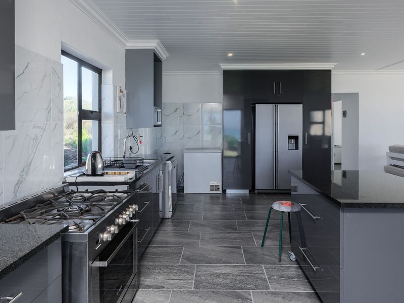 Modern kitchen featuring dark cabinetry, granite countertops, marble-look splashbacks, gas stove, and tiled flooring in an open-plan layout.