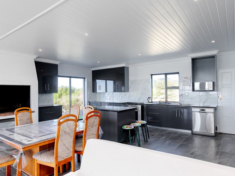 Spacious open-plan kitchen and dining area featuring modern dark cabinetry, a central island, built-in fireplace, and sleek tiled flooring with recessed lighting.