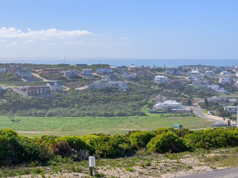 A wide-angle elevated view overlooking a coastal residential estate with natural vegetation and distant ocean horizon.