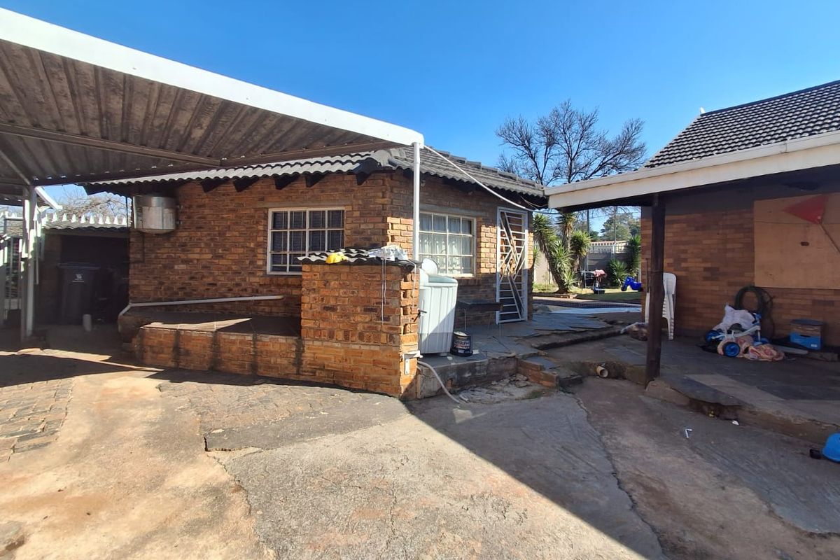 Rear exterior view of the property featuring a brick facade, covered patio area, and concrete paving, showing signs of wear and maintenance requirements.