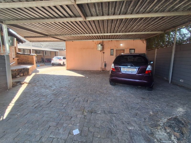 A covered carport area featuring a corrugated metal roof, paved flooring, and an external water heater unit.