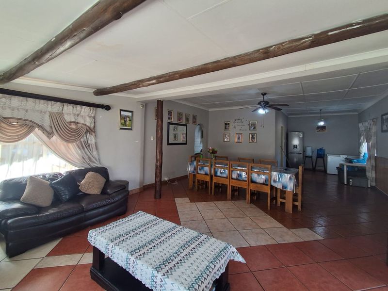 Spacious open-plan living and dining area featuring exposed timber ceiling beams, ceramic tile flooring, and a central ceiling fan.
