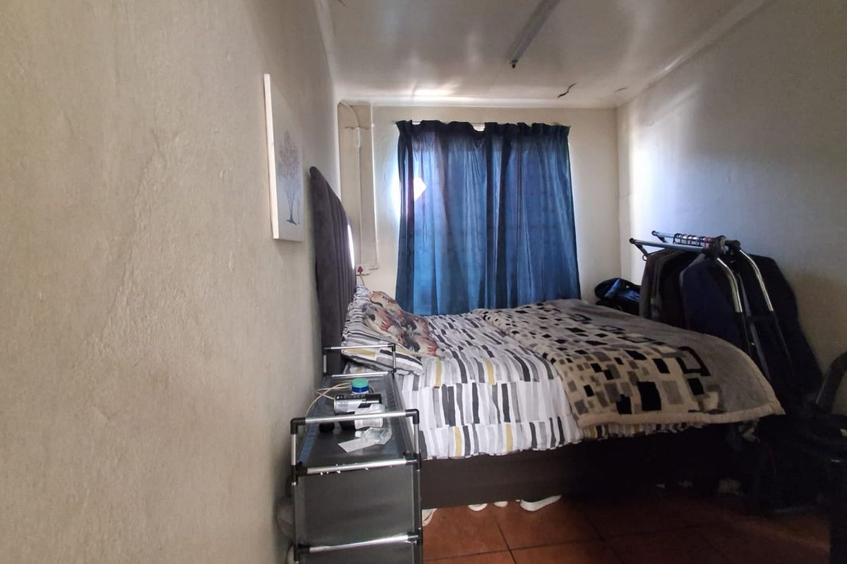A compact bedroom featuring tiled flooring and a ceiling light fixture, showing signs of wear including visible ceiling cracks.