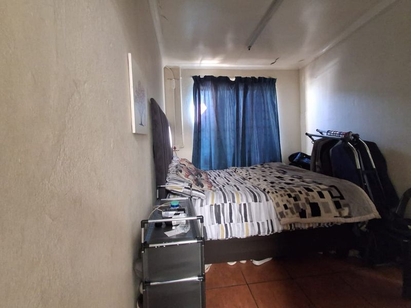 A compact bedroom featuring tiled flooring and a ceiling light fixture, showing signs of wear including visible ceiling cracks.
