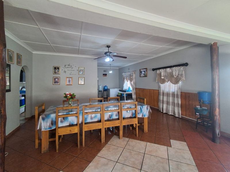 Spacious dining area featuring tiled flooring, wooden wall paneling, and a ceiling fan, offering a functional space for family meals.
