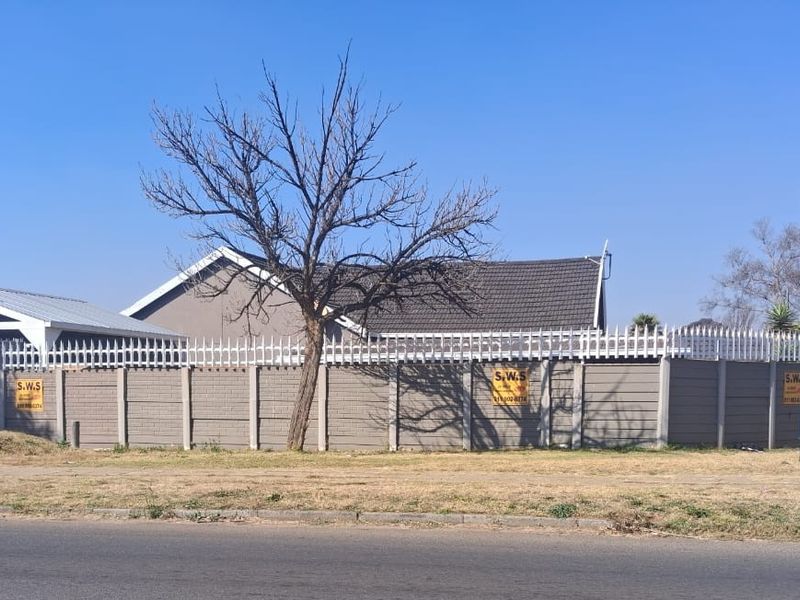 Front view of the property featuring a secure precast concrete boundary wall with spiked fencing and a detached garage structure.