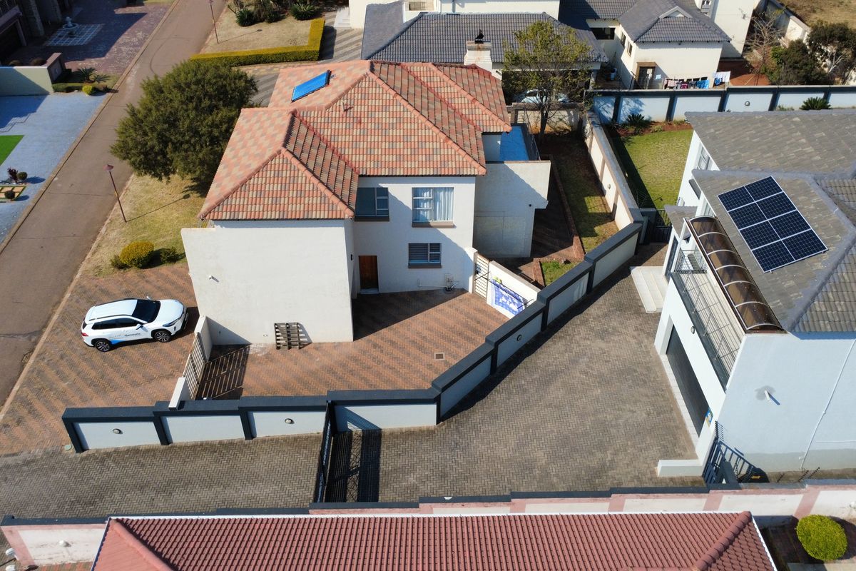 Aerial view of the property showing the main house, paved driveway, boundary walls, and roof-mounted solar panels.