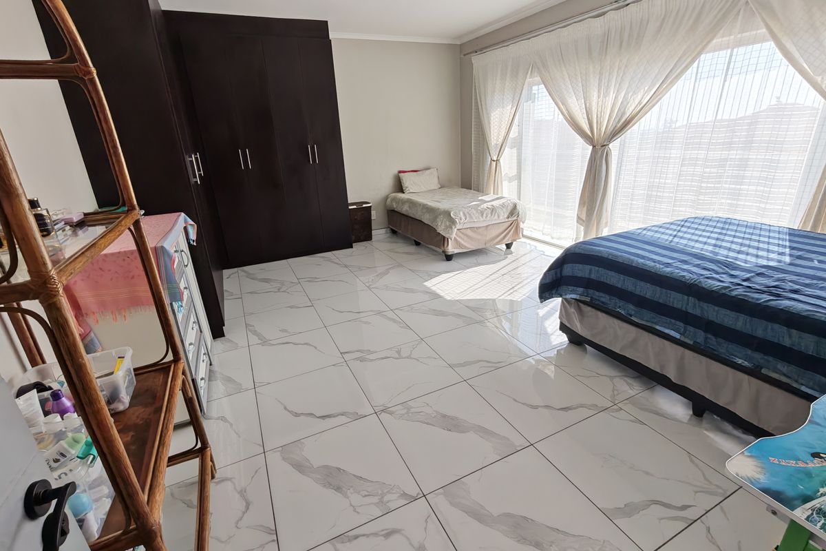 Spacious bedroom featuring large format marble-look porcelain floor tiles, extensive built-in cupboards, and a large sliding glass door providing ample natural light.