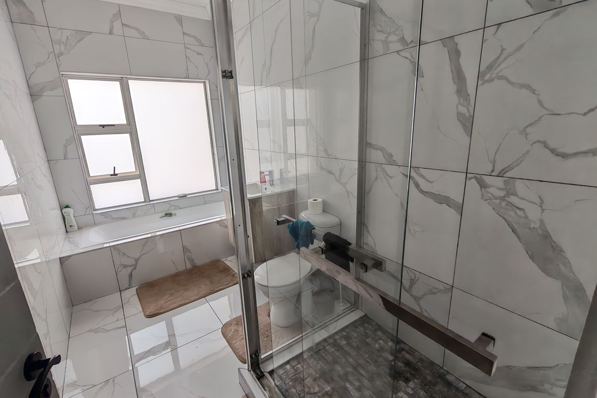 Modern bathroom featuring a glass-enclosed shower, built-in bathtub, and elegant marble-look wall tiling throughout.
